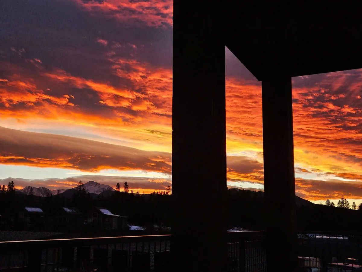 A stunning outdoor view at sunset, with vivid hues painting the sky above silhouetted mountain ranges and architectural pillars in the foreground. The tranquil scene captures the beauty of the natural setting and the relaxation that comes with evenings spent outdoors.