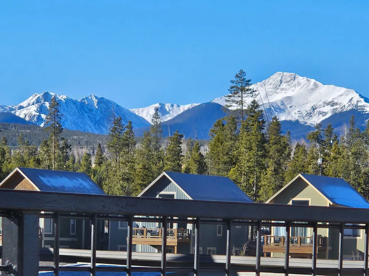 A picturesque view of snow-capped mountains, tall pine trees, and colorful cabins at the base, set under a bright sky. The scene hints at a variety of outdoor activities in every season, from hiking and skiing to nature walks.