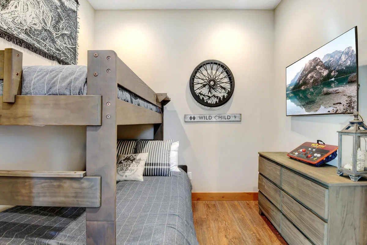 A welcoming bunk room is depicted, complete with a sturdy bunk bed, playful wall art, a dresser, and a television. The room exudes a youthful, playful vibe ideal for kids or extra guests, while maintaining a comfortable and inviting atmosphere.