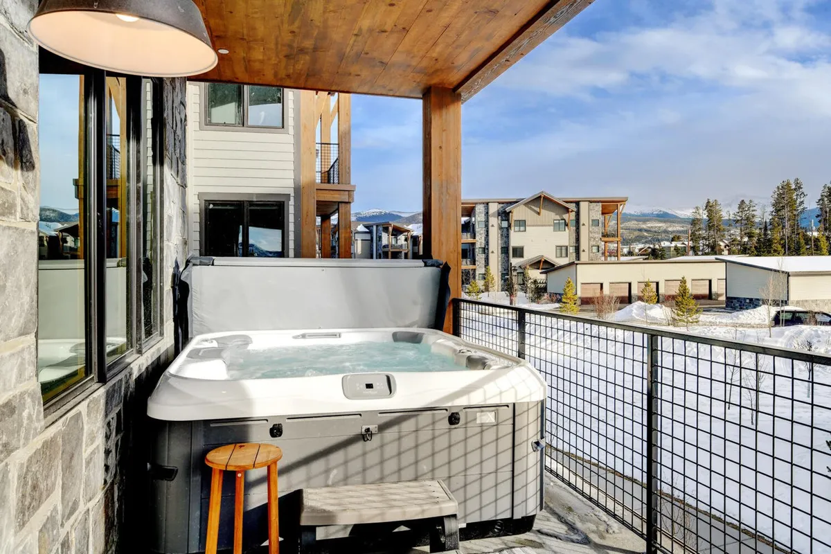 A serene outdoor hot tub set on a wooden deck with sweeping mountain views in the background. The setting is tranquil, inviting relaxation after a day of adventure, with the tub positioned to capture sunset colors and the surrounding natural scenery.