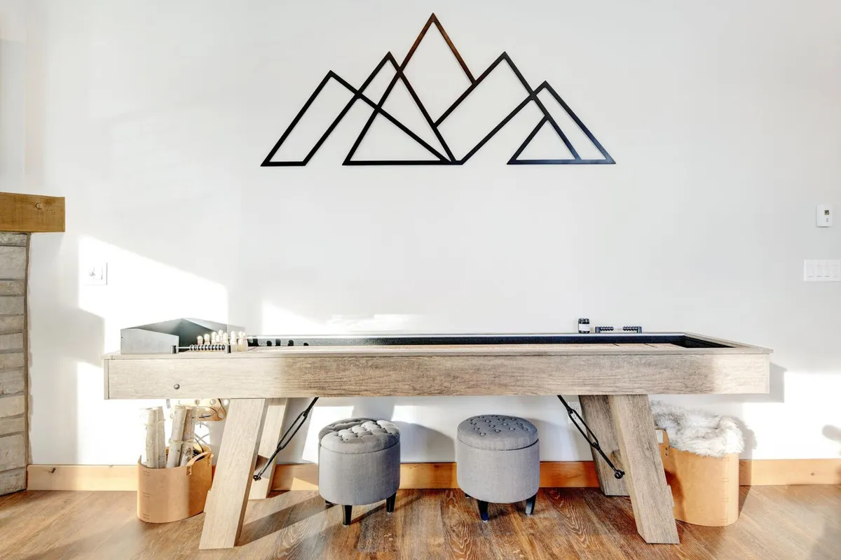 A fun game area centered around a shuffleboard table, complemented by mountain-themed wall art and comfortable round stools. The casual atmosphere is ideal for lively family competitions and friendly socializing.