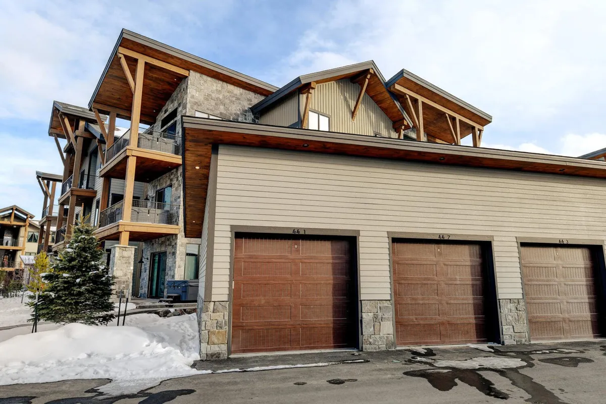 The exterior of the property features striking wooden beams, a rustic stone facade, and inviting garage doors, all set against a picturesque mountain backdrop. Hints of social spaces and balconies suggest areas for enjoying the outdoors and gathering with friends or family.