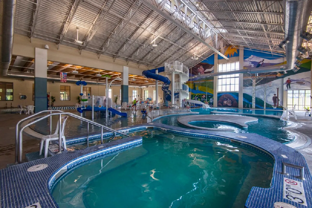 A lively indoor scene at the Grand Park Rec Center’s aquatic facility, featuring water slides, play structures, and swimming areas, all filled with joyful families and children. The space is colorful and bustling with energy.