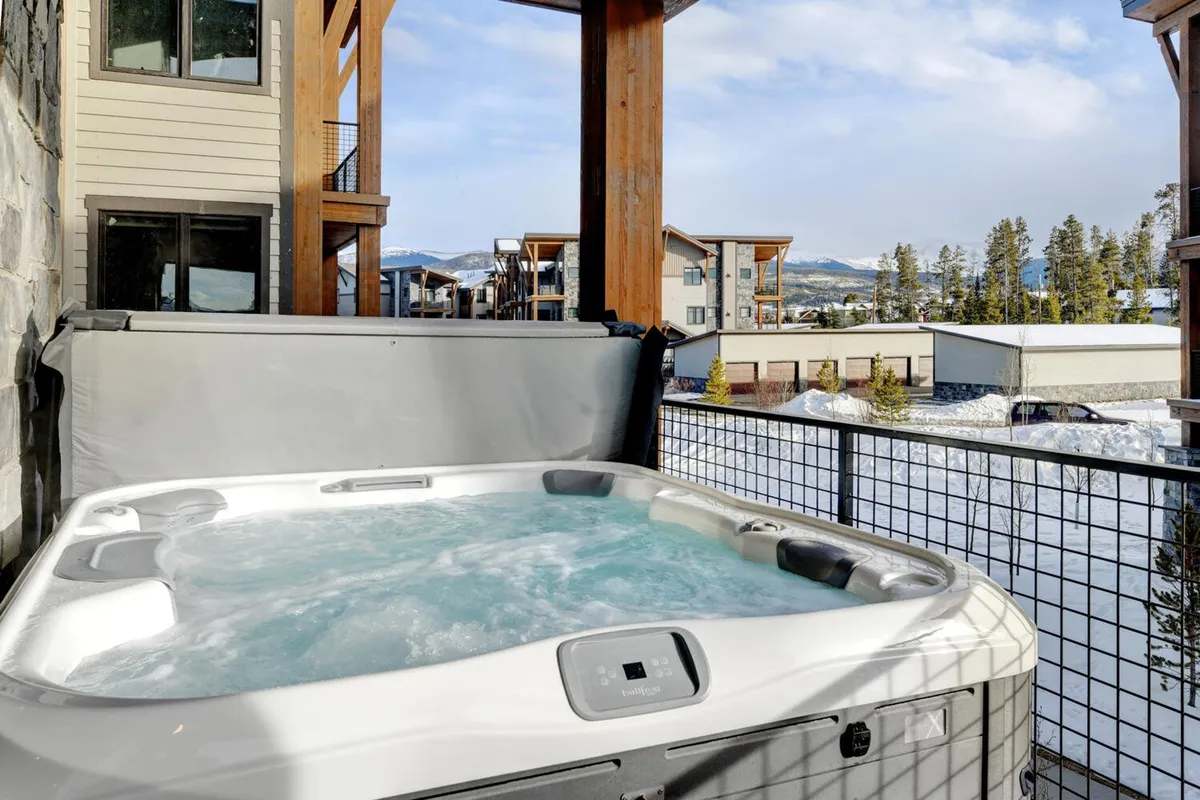 This exterior image features a welcoming hot tub on a balcony, with expansive mountain views and surrounding architecture that hint at a communal, outdoor gathering space. The tranquil setting is perfect for relaxing after a day of group activities, and the balcony area suggests an ideal spot for sharing meals or drinks with friends or family while soaking in the scenery.