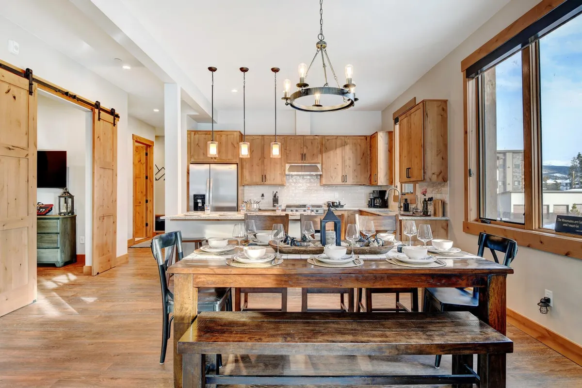 A dining area set for a meal, adjacent to the kitchen cabinetry and featuring large windows that fill the space with light. The table is arranged for a group, signaling readiness for family dinners or festive gatherings, with an inviting, social atmosphere.