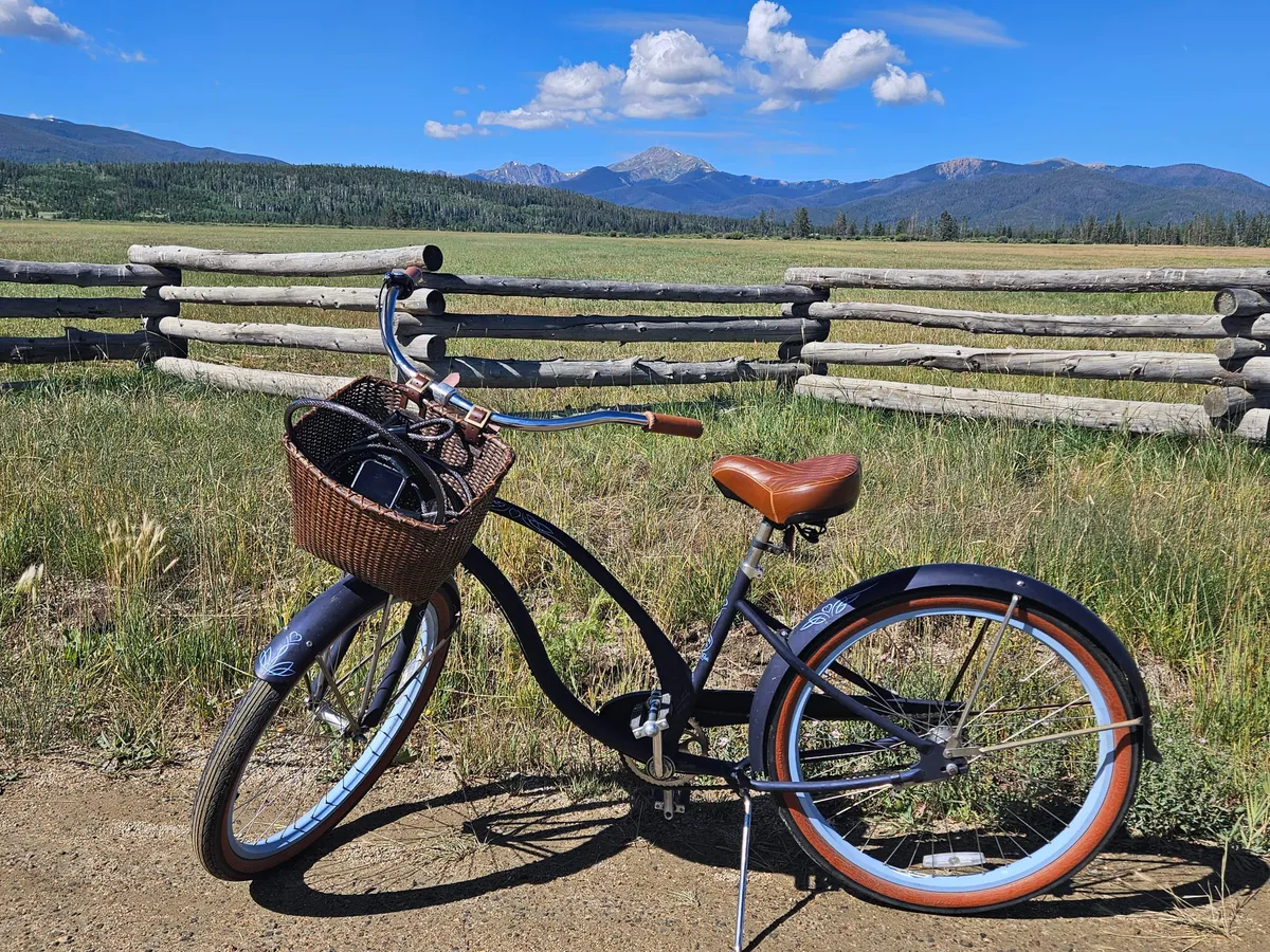 A scenic exterior shot of a bicycle leaning against a wooden fence, looking out over a sweeping mountain landscape. The relaxed mood and open space invite thoughts of outdoor exploration and biking.