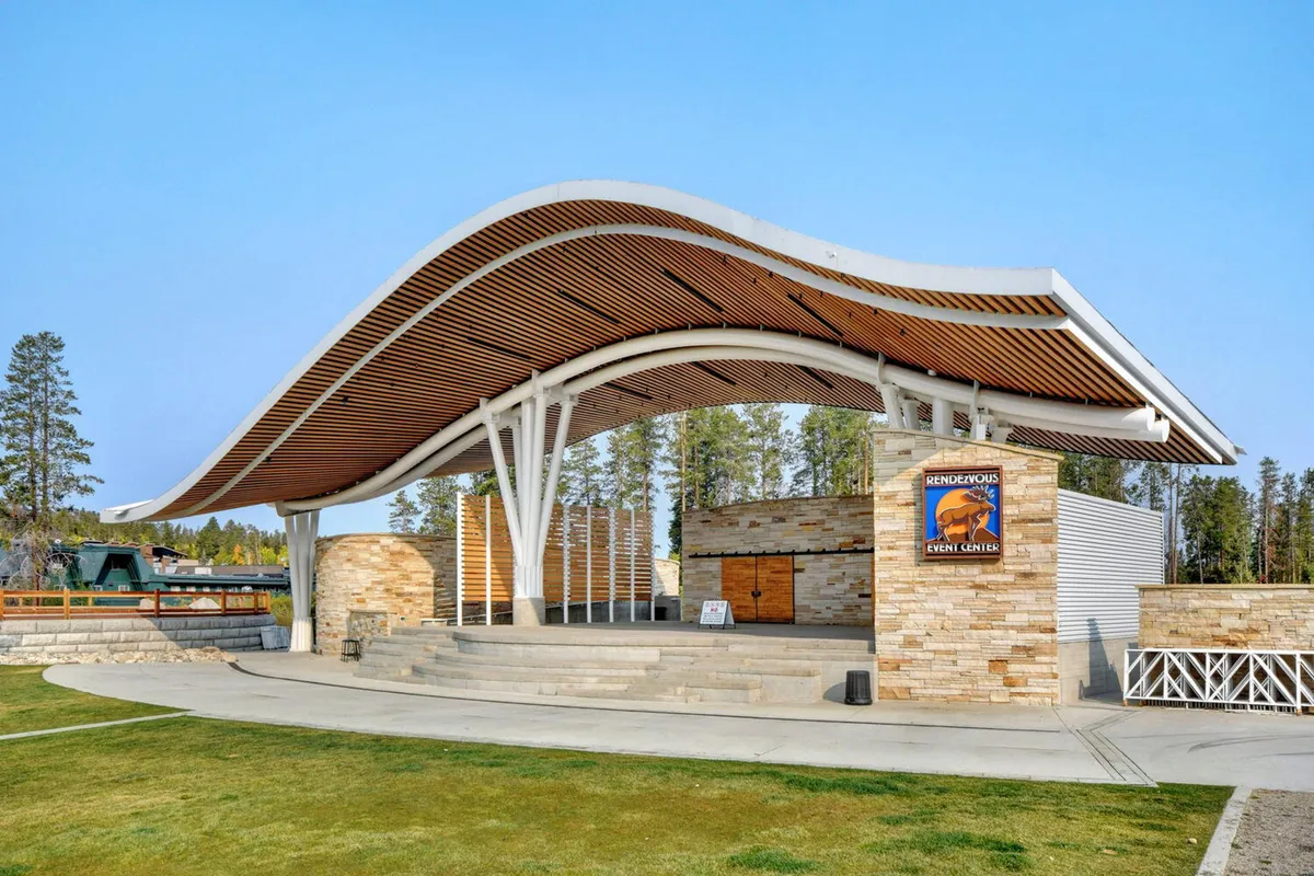 An exterior shot of the Hideaway Park amphitheater, showcasing its unique curved roof structure, stone facade, and wooden accents. The image hints at outdoor performances and community events, aligning with the section’s mention of concerts and gatherings just steps from the home.