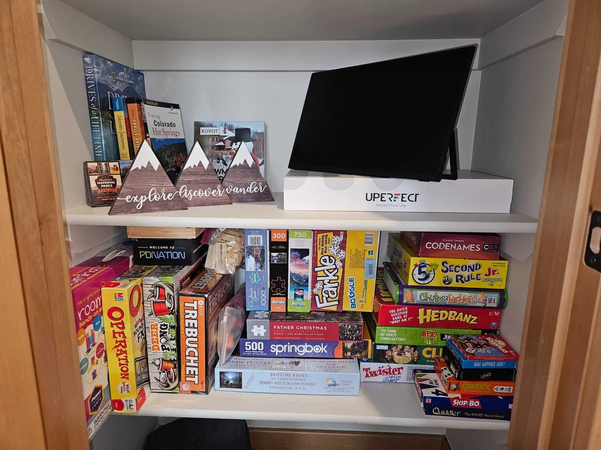 A shelf brimming with a diverse collection of board games, along with books and a cheerful decorative sign. The cozy vibe encourages group play and family traditions.