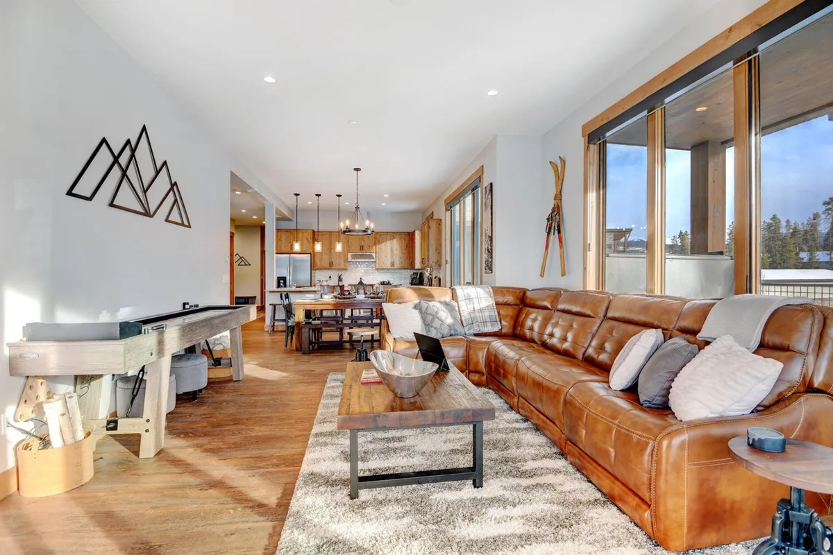 A welcoming interior living space with a large leather sofa, dining area, and expansive windows displaying mountain views. The room exudes comfort, and the setup is perfect for family movie nights, board games, and cozy evenings together.