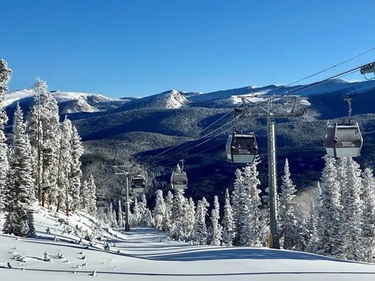 The image captures ski lift gondolas moving up a snow-covered mountain landscape, with pine trees and distant peaks in view. The bright, clear sky and pristine snow emphasize a sense of adventure and the winter sports atmosphere.