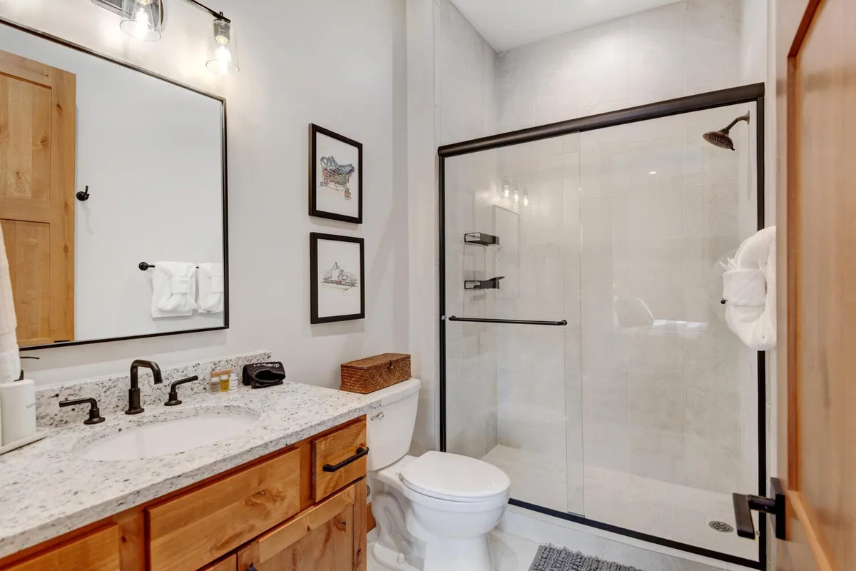 A luxurious bathroom scene with a granite countertop, glass shower enclosure, framed artwork, and wooden cabinetry. The mood is tranquil and spa-like, reinforcing the sense of comfort and relaxation prevalent throughout the accommodation.